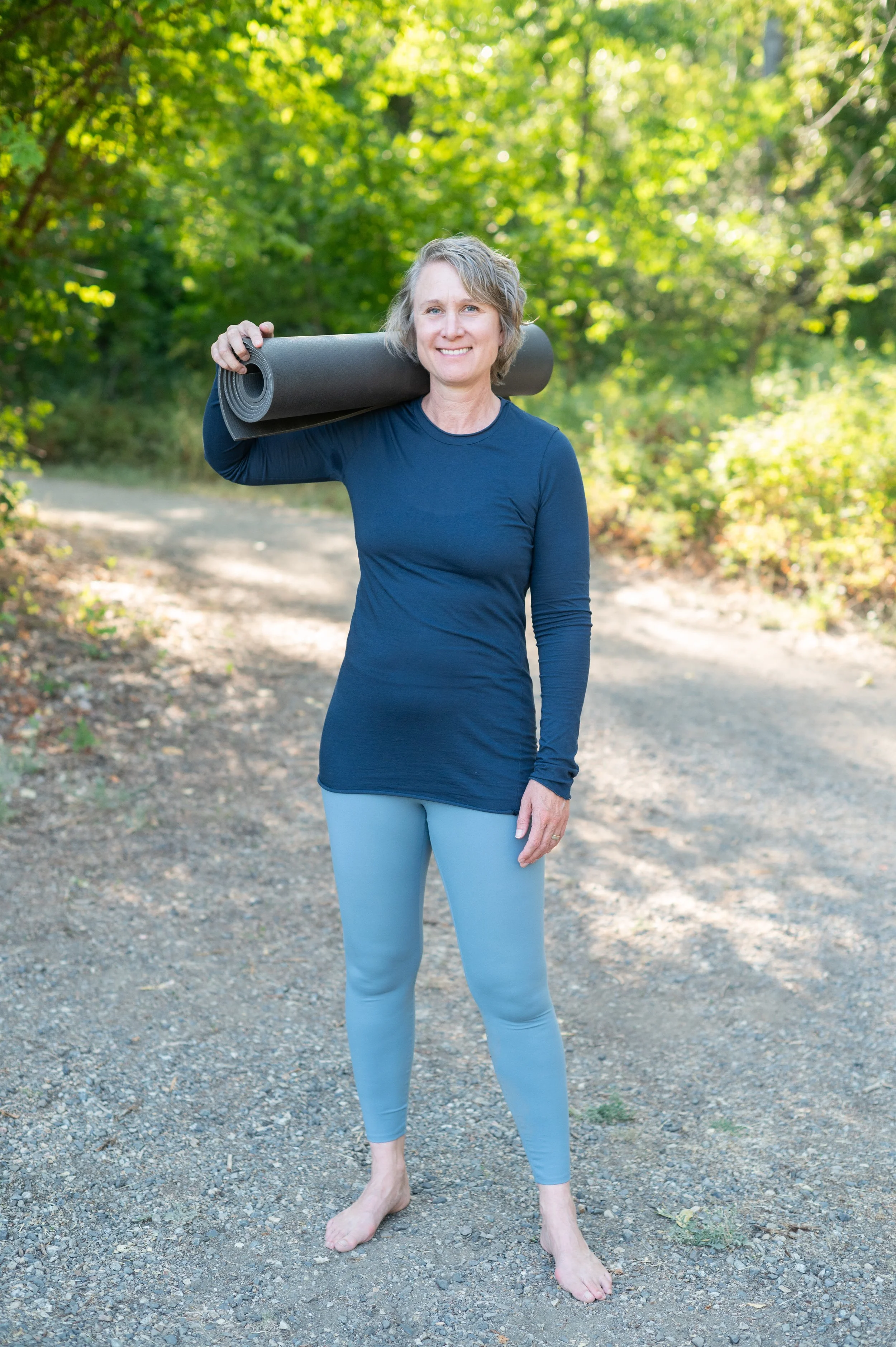 woman in blue workout clothes holding a yoga mat on her shoulder