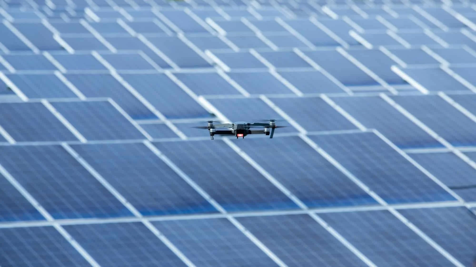 A drone flying over a large array of blue solar panels performing an aerial thermal inspection in Maine of a solar farm, PV array, CSF, solar utility power plant producer.