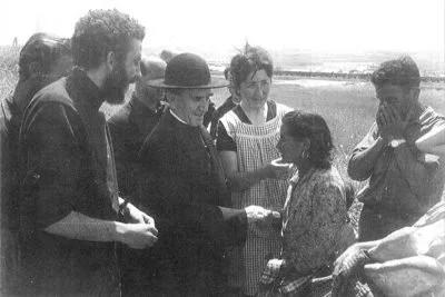 Grupo de cinco personas en un campo, con una mujer entregando un objeto a otra mujer.