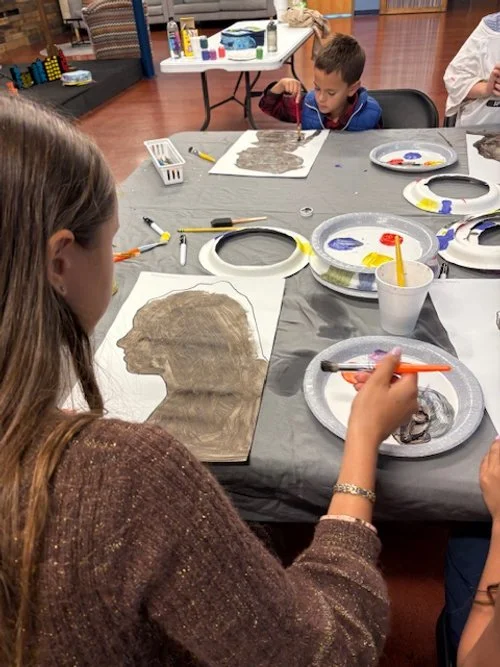 Children working on art projects with animal silhouette templates, paint, and brushes on a table.