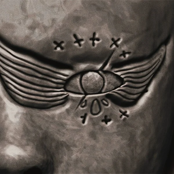 Close-up of a tattoo depicting an eye with wings, surrounded by 'X' marks and the number '100' underneath.
