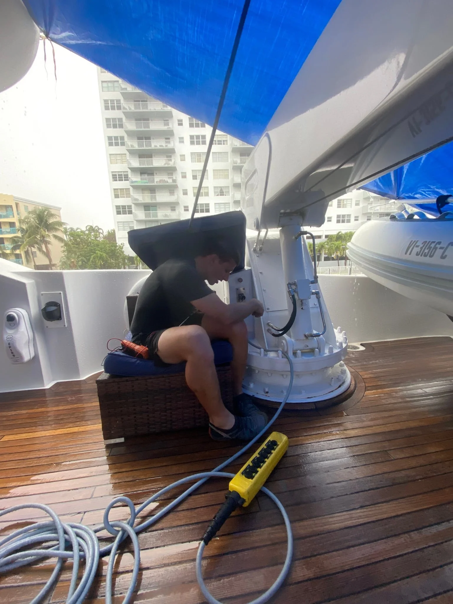 A technician servicing on a yachts crane, with multiple electrical cords and plugs connected.