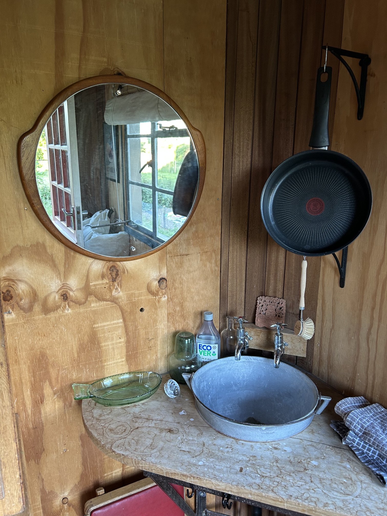 Rustic wash basin with mirror and hanging pan in shepherd's wagon kitchen
