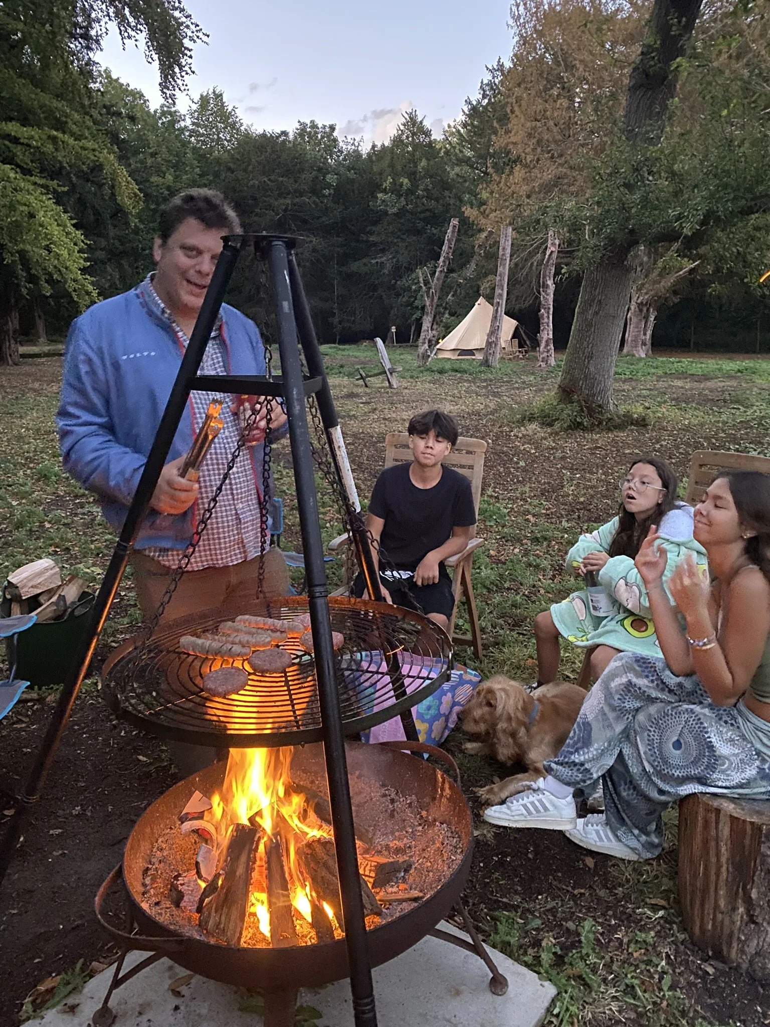Family grilling dinner over fire pit at woodland campsite