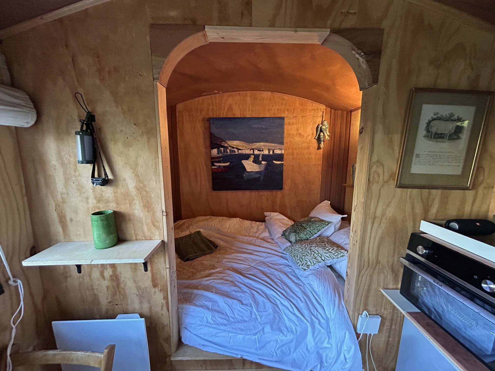 Interior of shepherd's wagon showing dining table, bed and kitchen, woodland view
