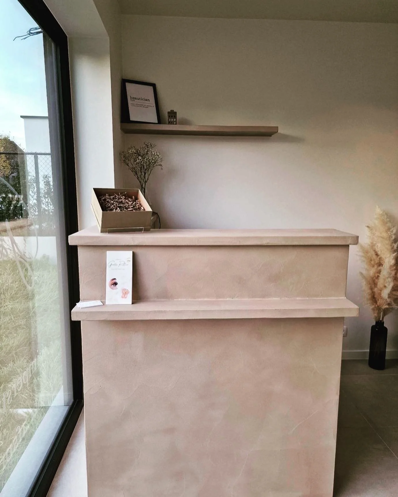 Op maat gemaakte receptiebalie in zachte roze microcement afwerking voor schoonheidssalon