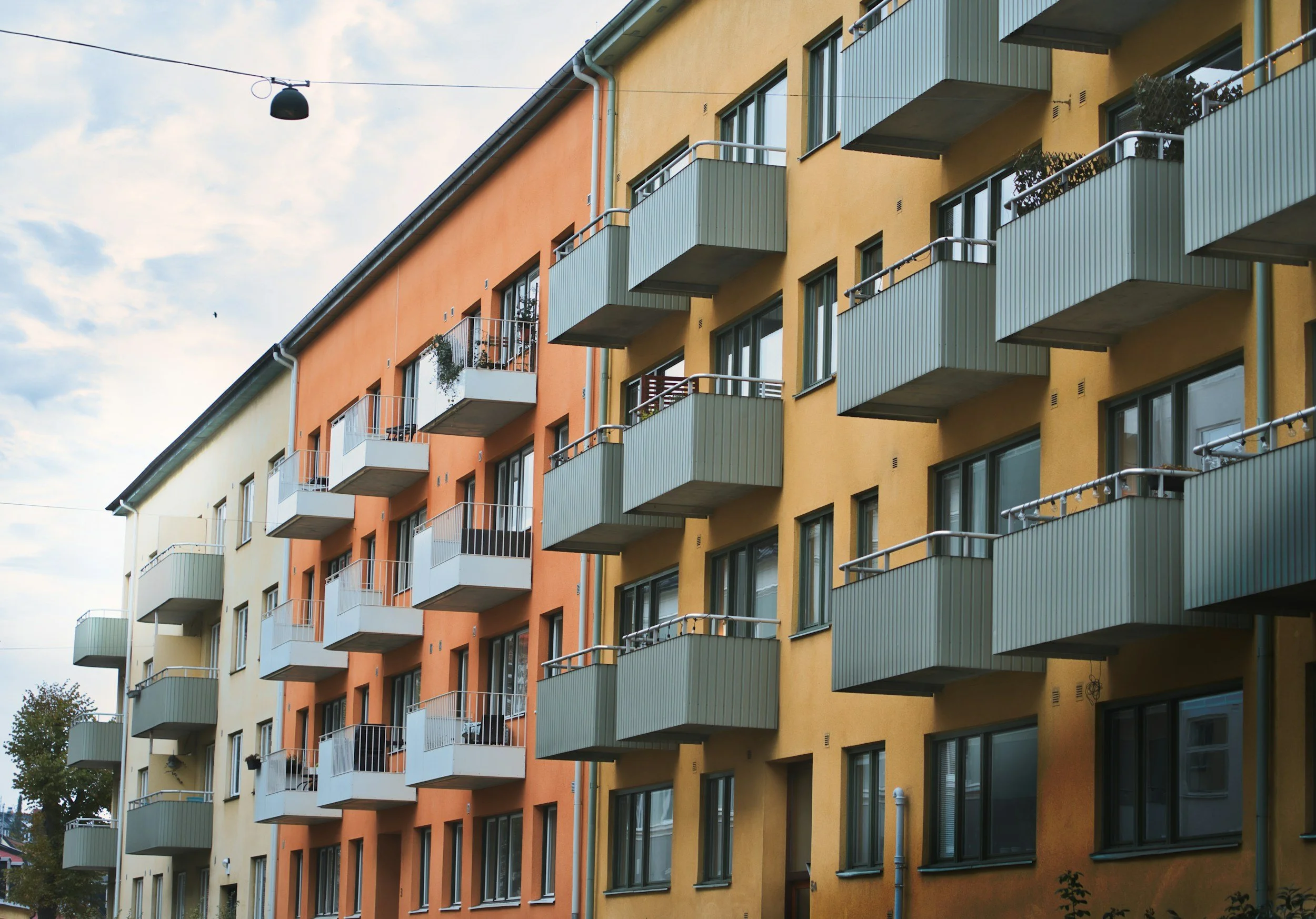 Multi-story apartment building with balconies, painted in yellow and orange, with a cloudy sky above.