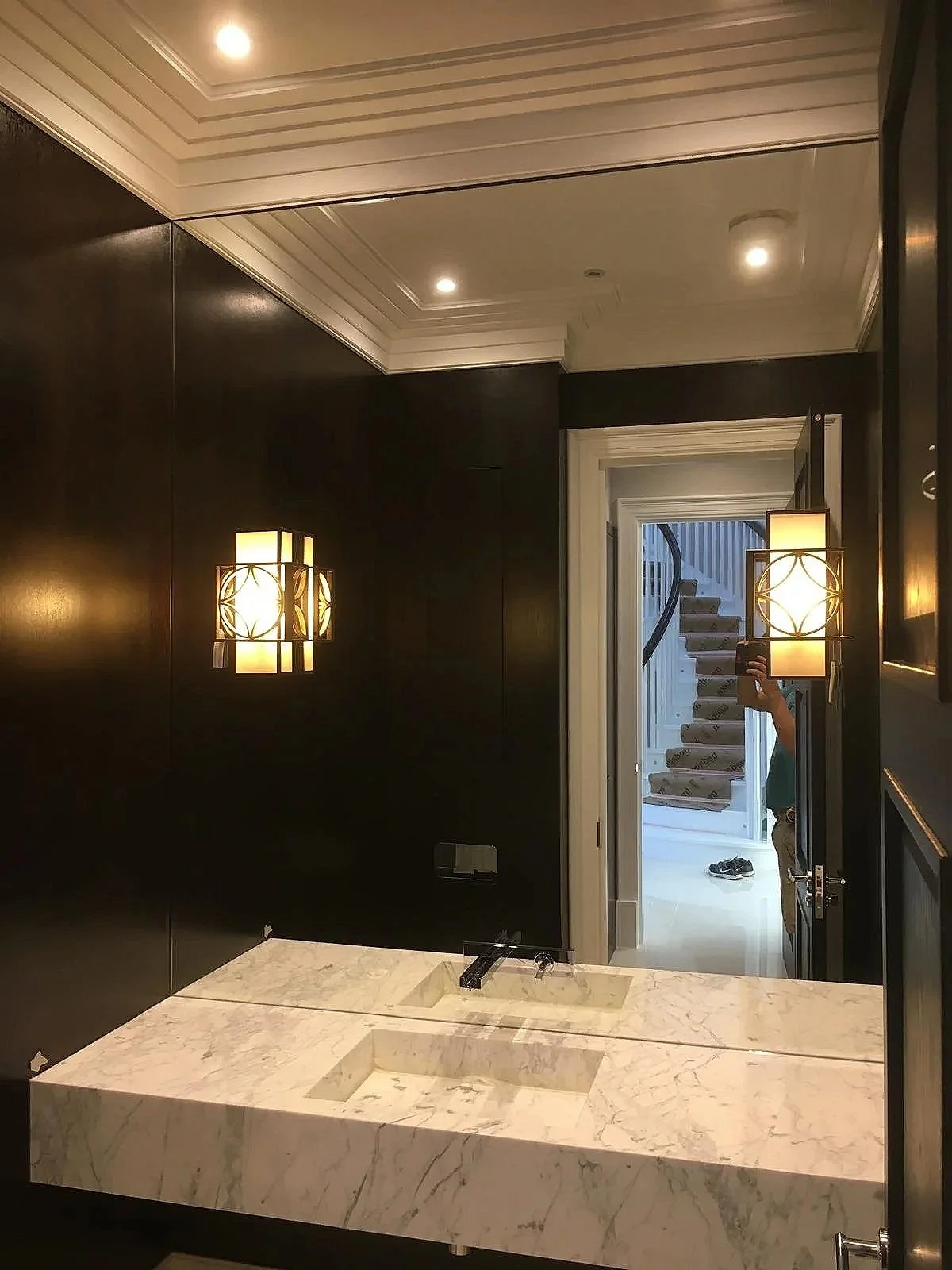 Bespoke bathroom mirror fitted above vanity sink with contemporary wall lighting and tiled feature wall in a modern Surrey home.