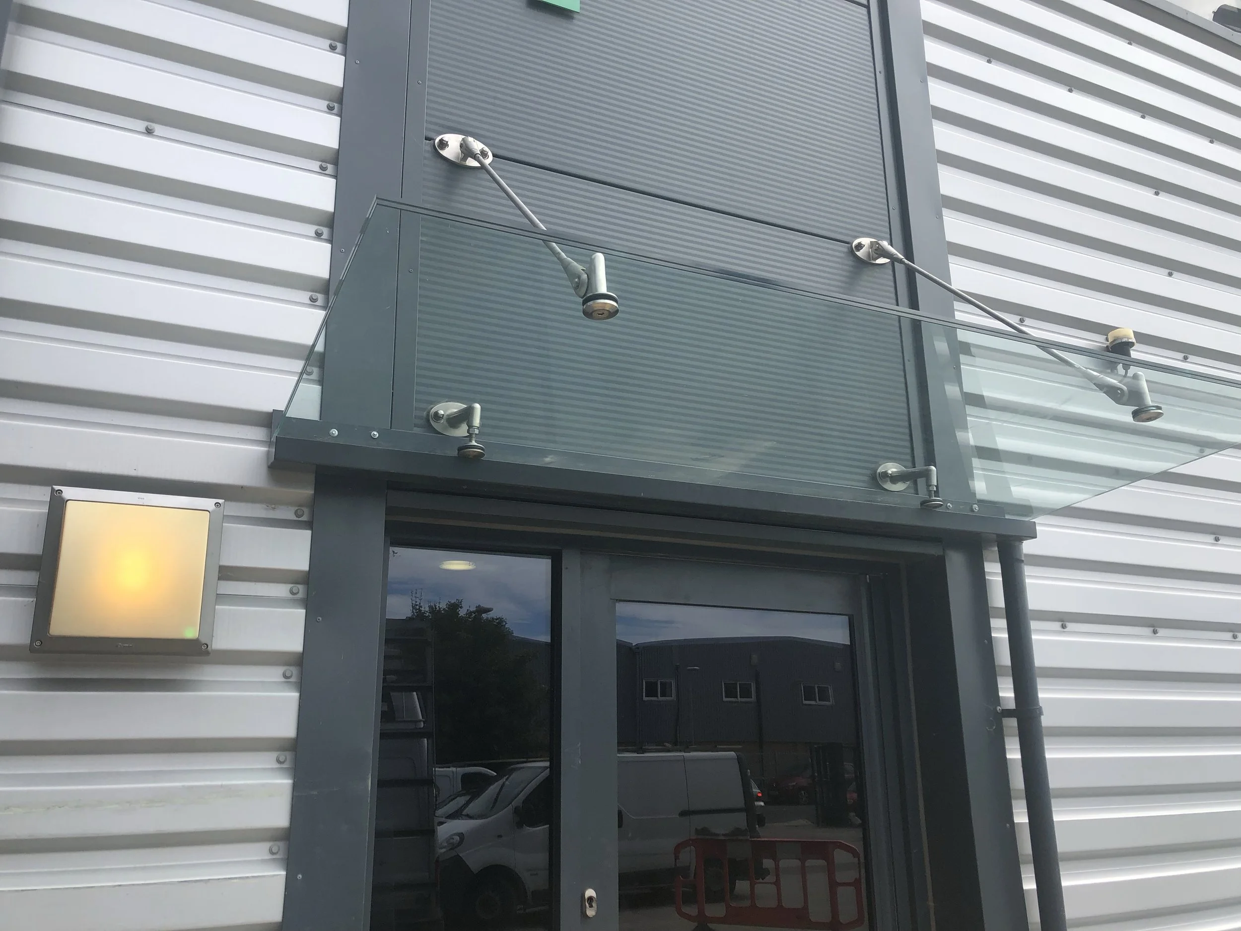 Bespoke glass canopy fitted above a custom-sized entrance, designed with stainless steel rod supports and clear toughened glass. surrey