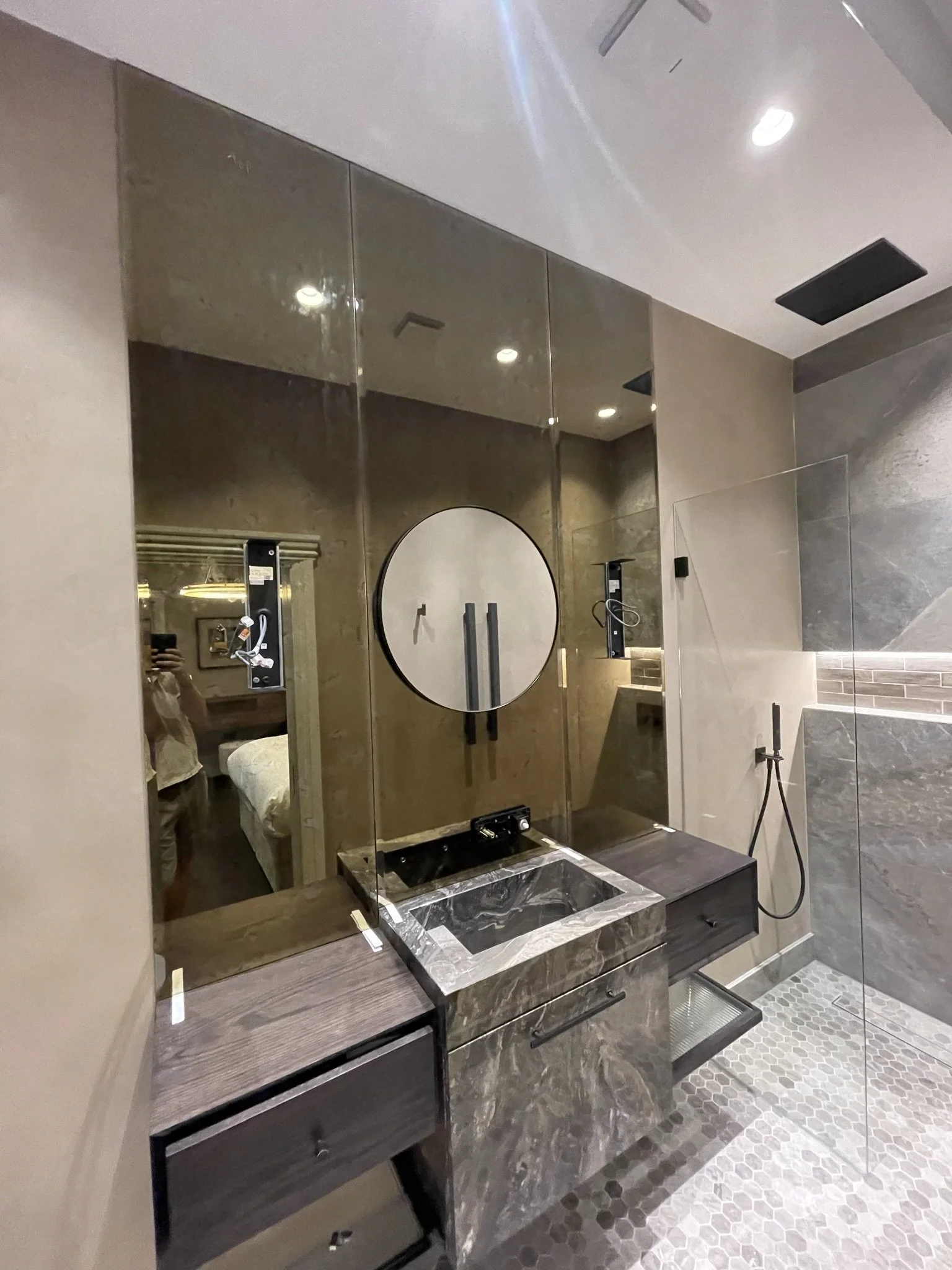Tinted bronze mirror with tap cut-outs and drill holes, supplied and fitted in luxury bathroom at Palace Gate, London. Installed using specialist mirror adhesive next to custom shower screen.