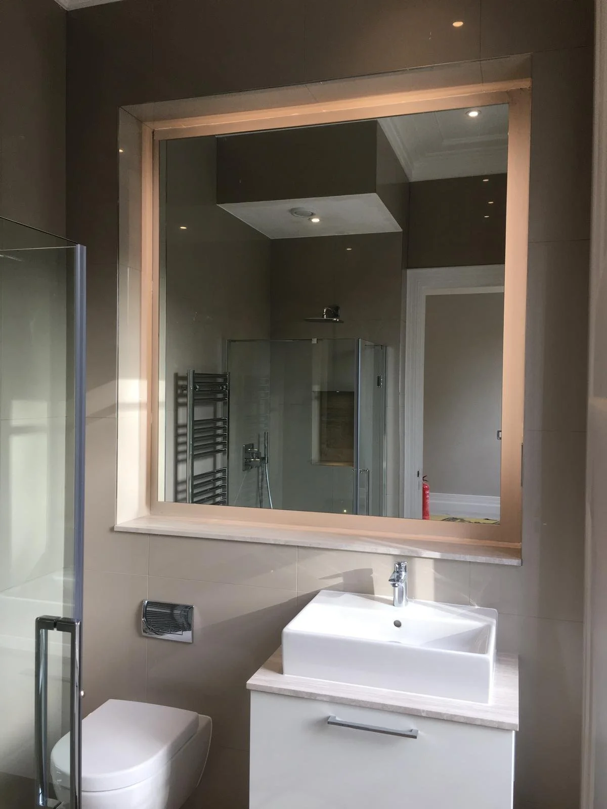 LED backlit bathroom mirror installed in a modern shower room above vanity basin with contemporary lighting and tiled feature wall.