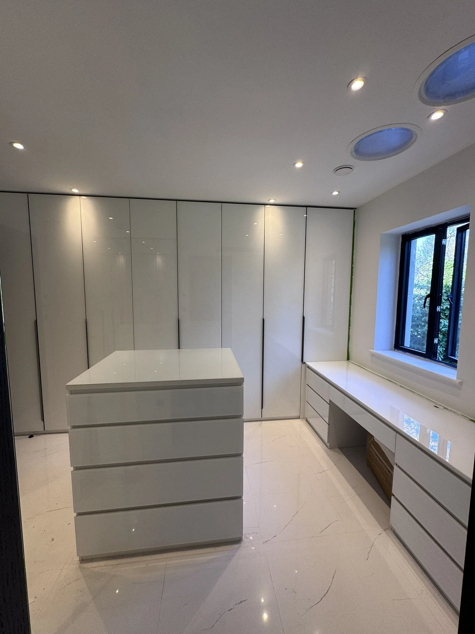 Back-painted low iron glass wardrobe doors, glass desktop and island installation in a bespoke dressing room in Kingston Hill