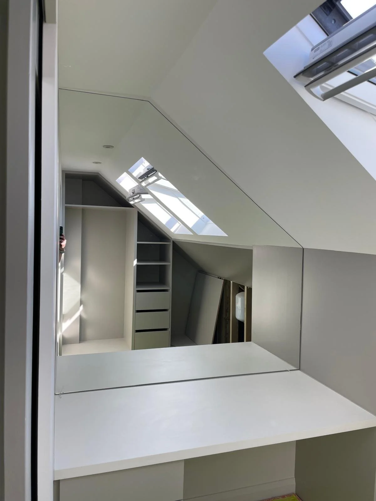 Custom shaped mirror fitted inside a loft conversion wardrobe area with angled ceiling, designed and installed by Hamilton Glass Products Surrey.