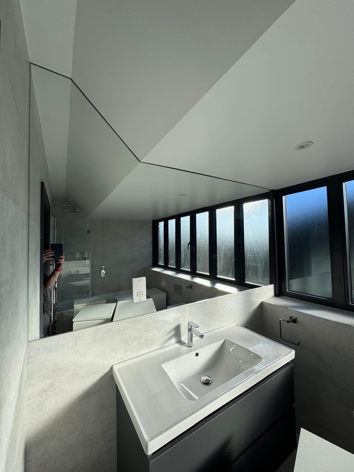 Custom shaped mirror cut to fit a feature wall and architectural angles in a contemporary interior installation.