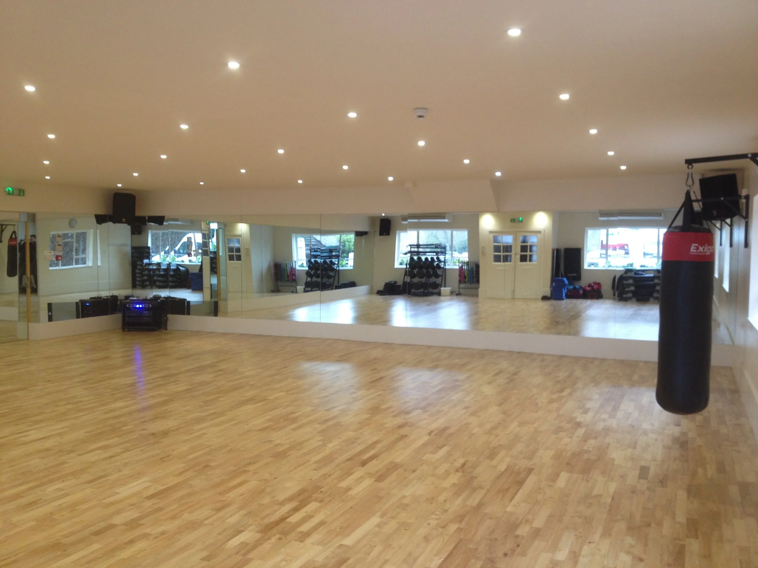 Large commercial gym mirror wall installation providing full room reflection for exercise classes and fitness training studios.
