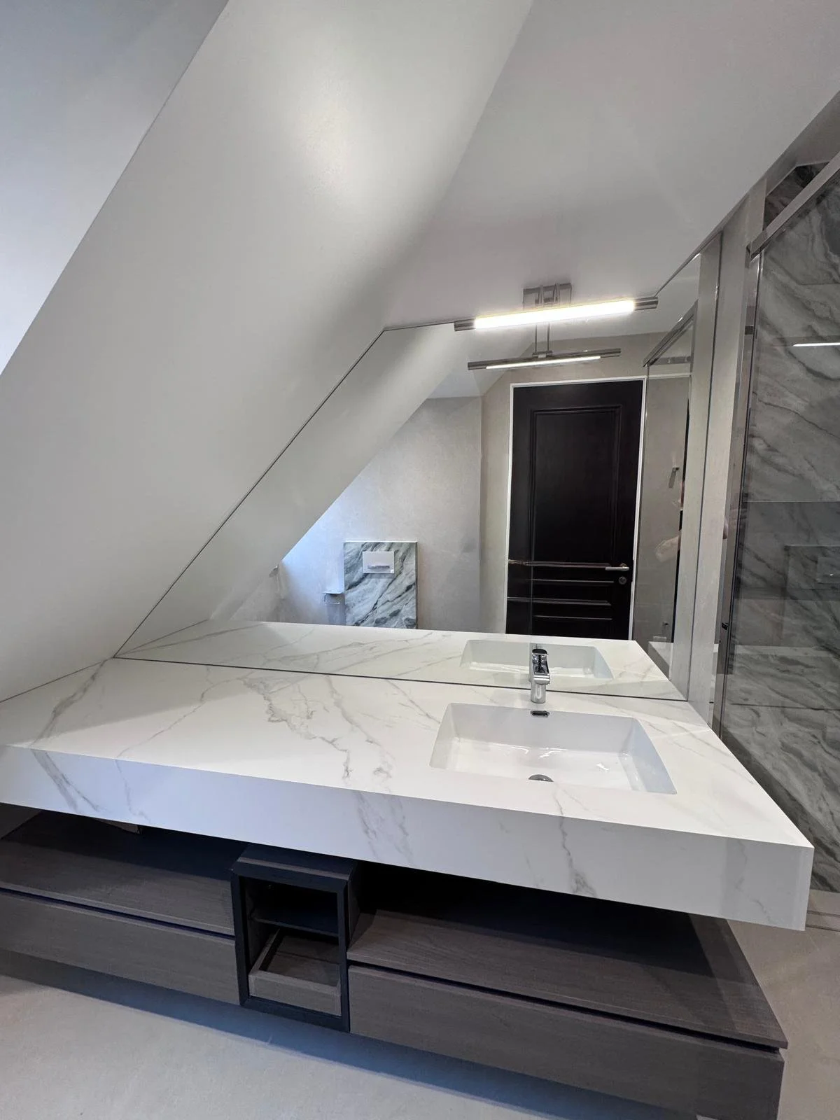 Custom shaped mirror fitted inside a loft conversion wardrobe area with angled ceiling, designed and installed by Hamilton Glass Products Surrey.