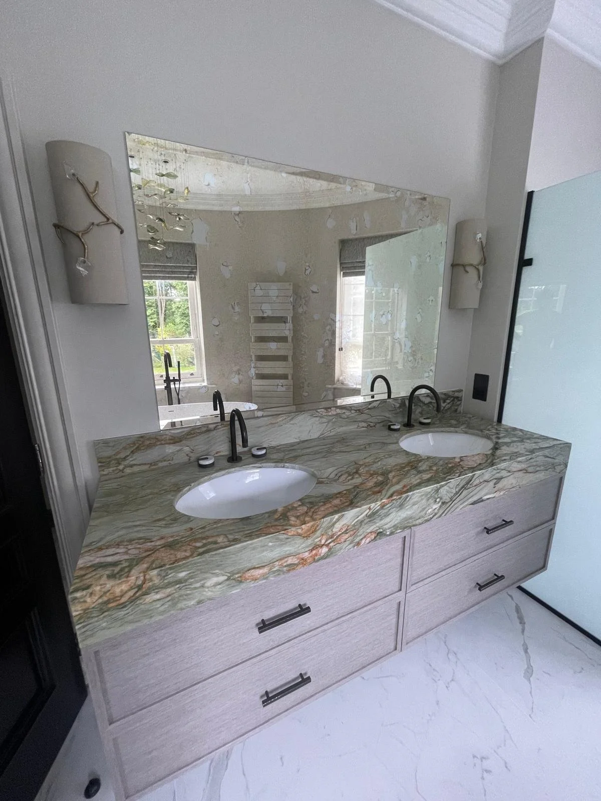 Large frameless mirror with LED backlighting installed above a modern vanity sink in a designer bathroom.