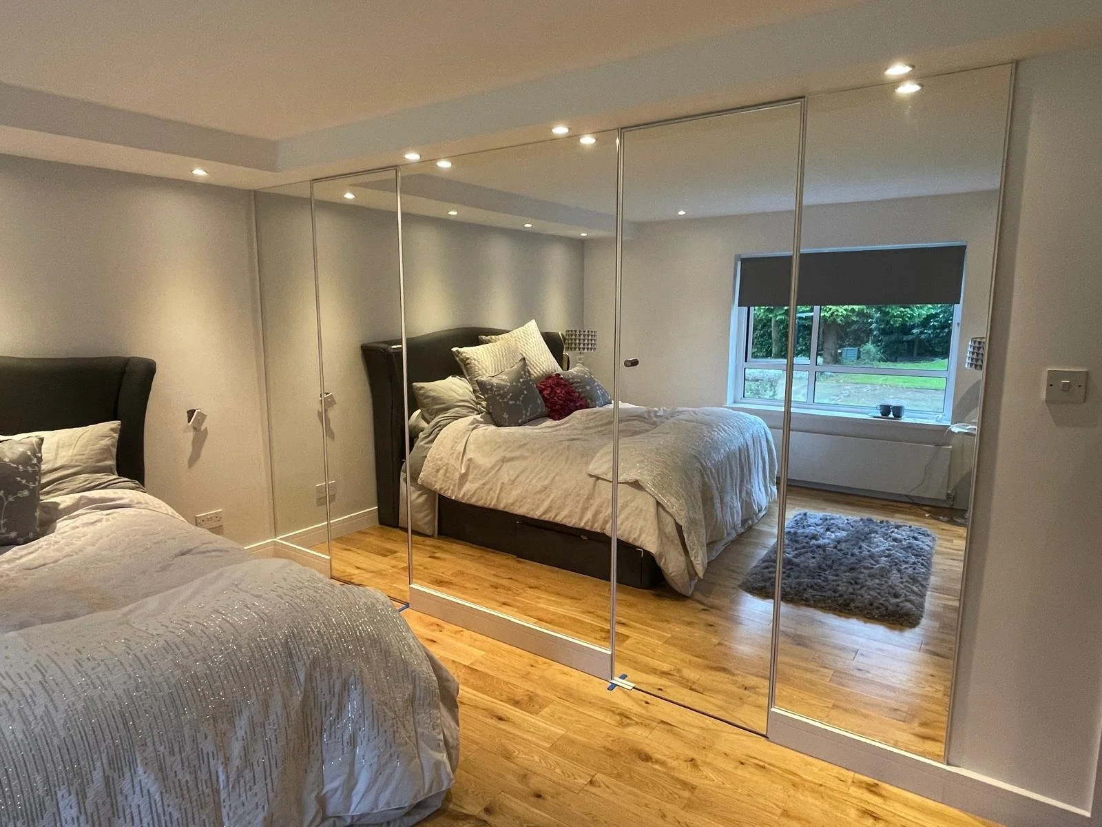 Mirrored wardrobe doors installed floor to ceiling creating a large reflective surface and brightening a modern bedroom interior.