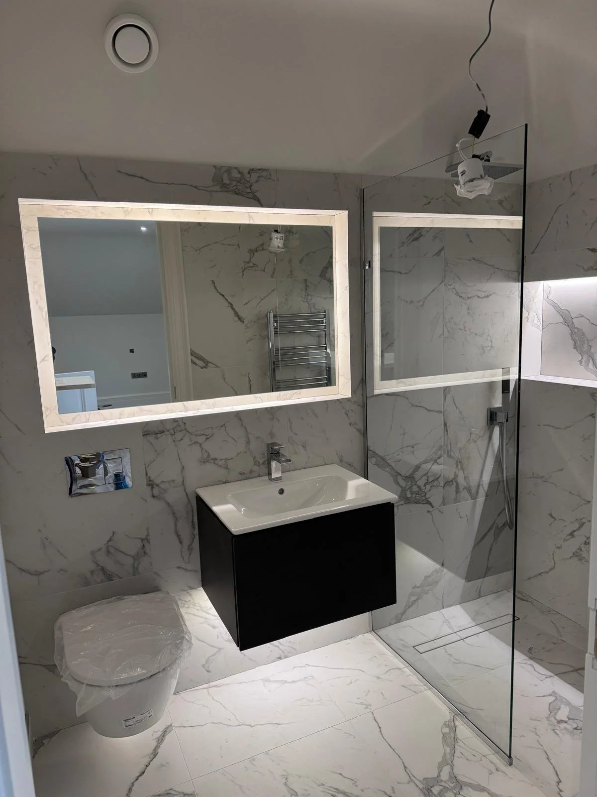 Large wall mirror fitted above a floating vanity basin with recessed shelving and modern bathroom storage.