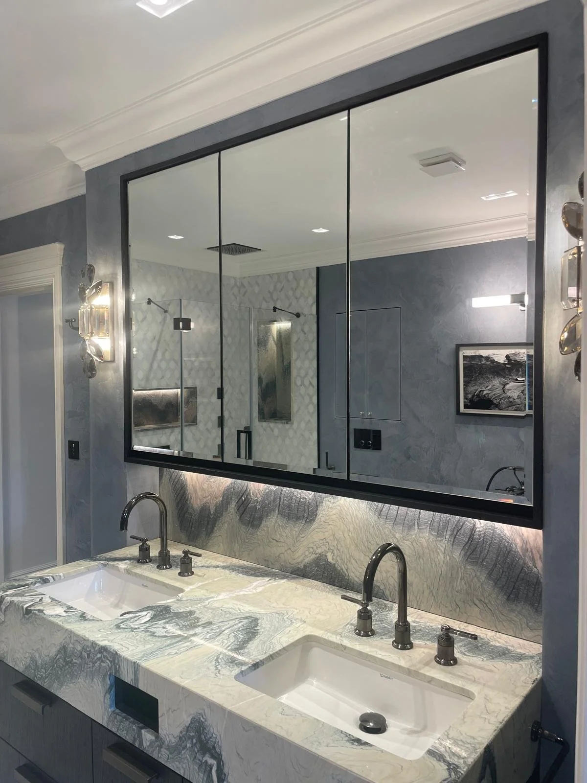 Bespoke bathroom vanity mirror installed above sink unit with overhead cupboard doors and integrated storage in a modern Surrey bathroom.