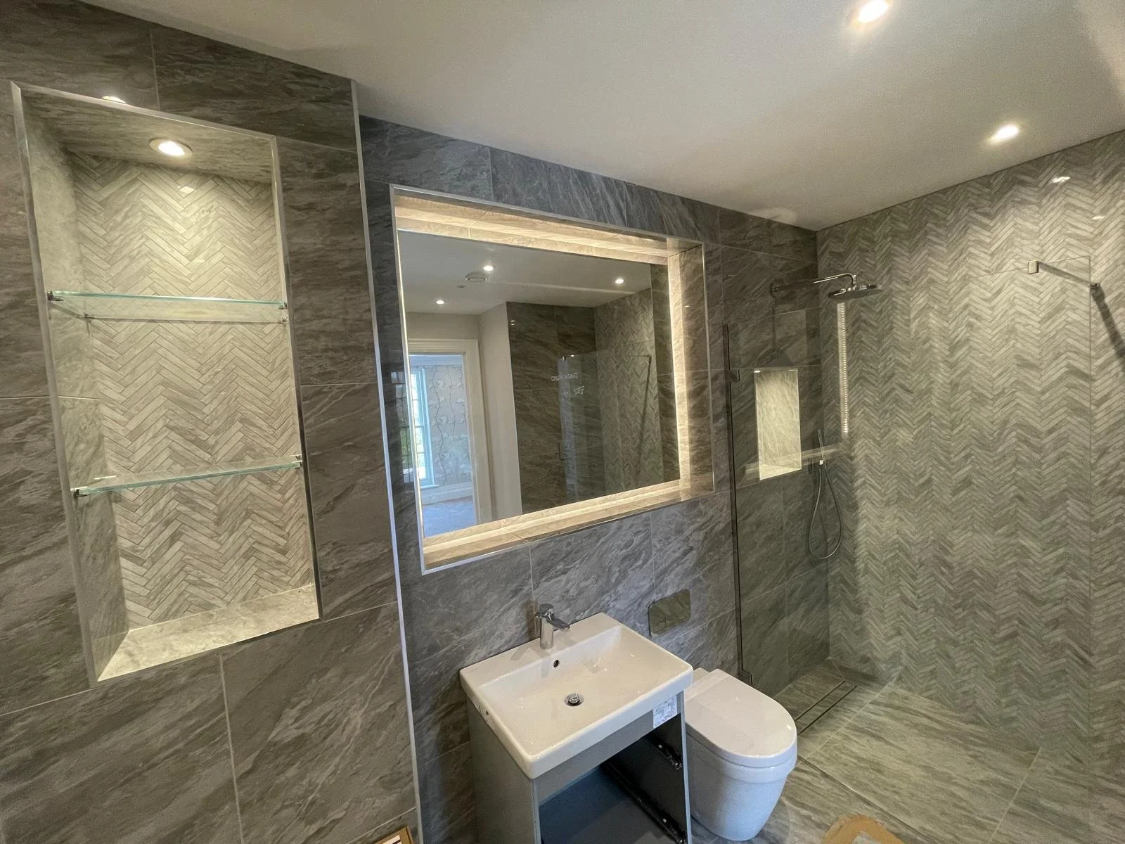 Large frameless mirror with LED backlighting and toughened shelves  installed above a modern vanity basin providing ambient lighting and a luxury bathroom finish.
