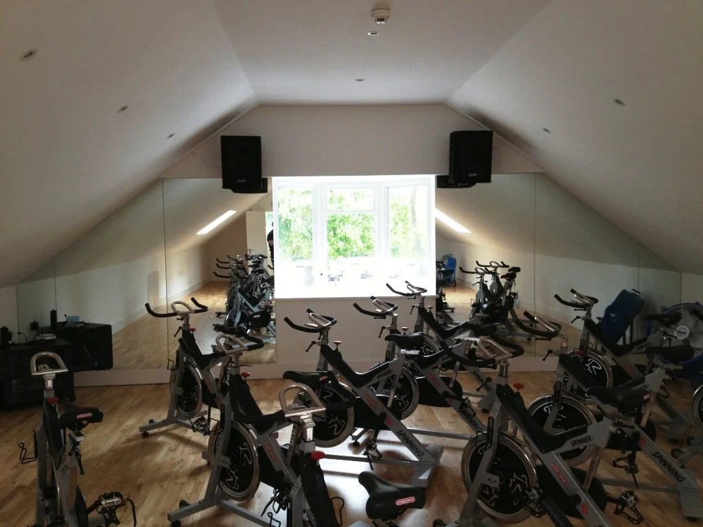 Custom wall mirrors installed in a loft gym with angled ceilings, providing a full reflection training area for indoor cycling and fitness workouts.