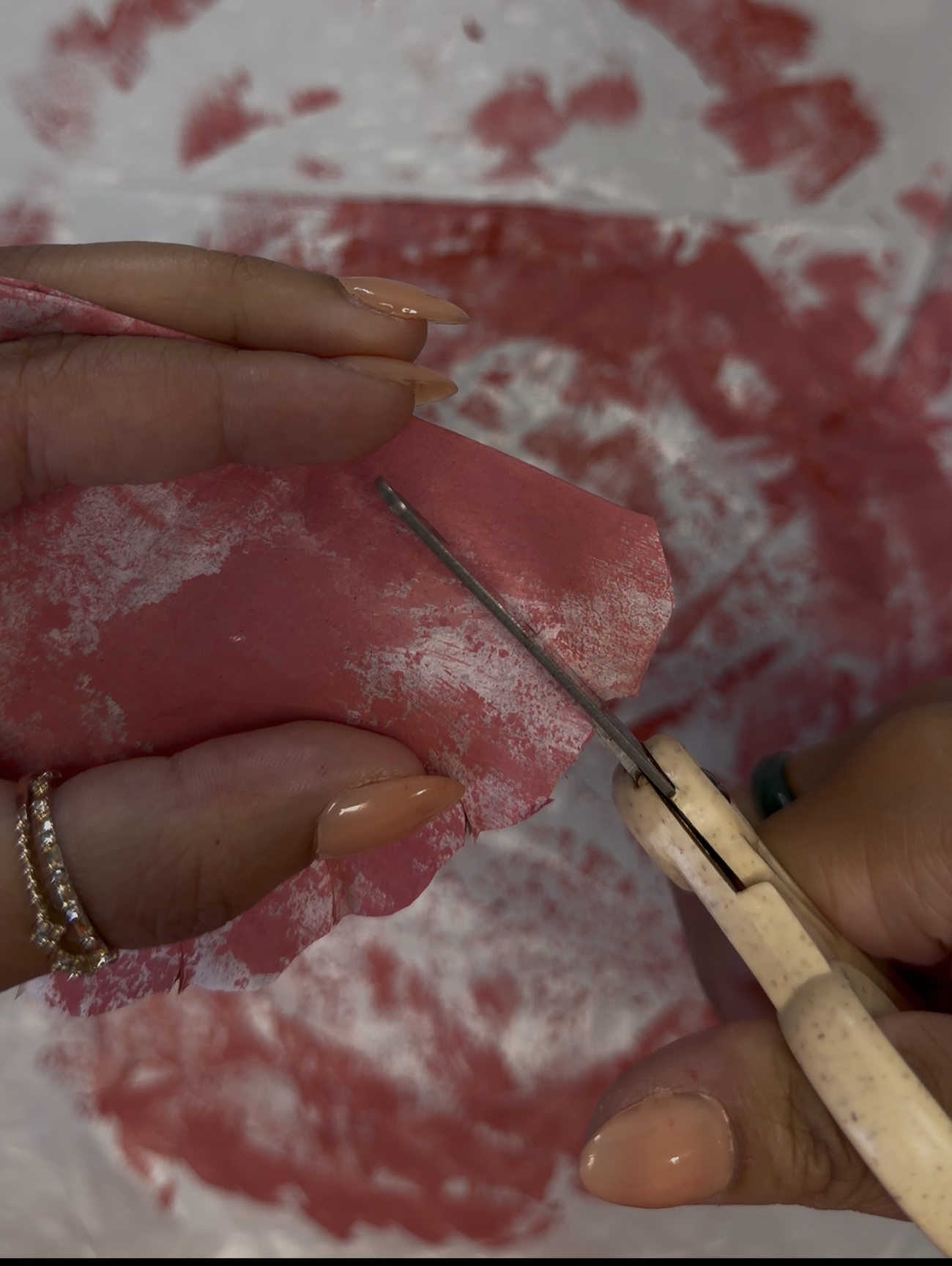 Close-up of scissors cutting small slits into a painted coffee filter to create realistic paper flower petals