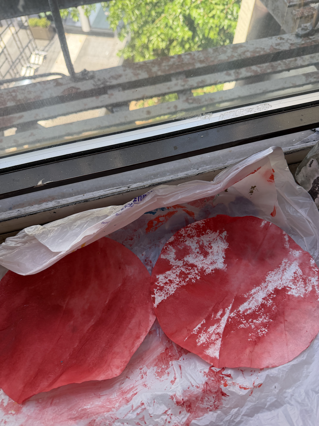 Hand-painted pink coffee filters drying on a sunny windowsill before being turned into paper peony flowers