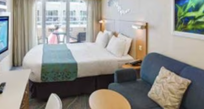 A hotel room with a large bed, a blue sofa, a window with curtains, and a painting on the wall.
