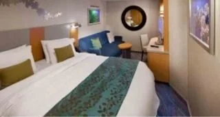 Hotel room with a large bed, two pillows, a blue sofa, a lamp, and artwork on the walls.