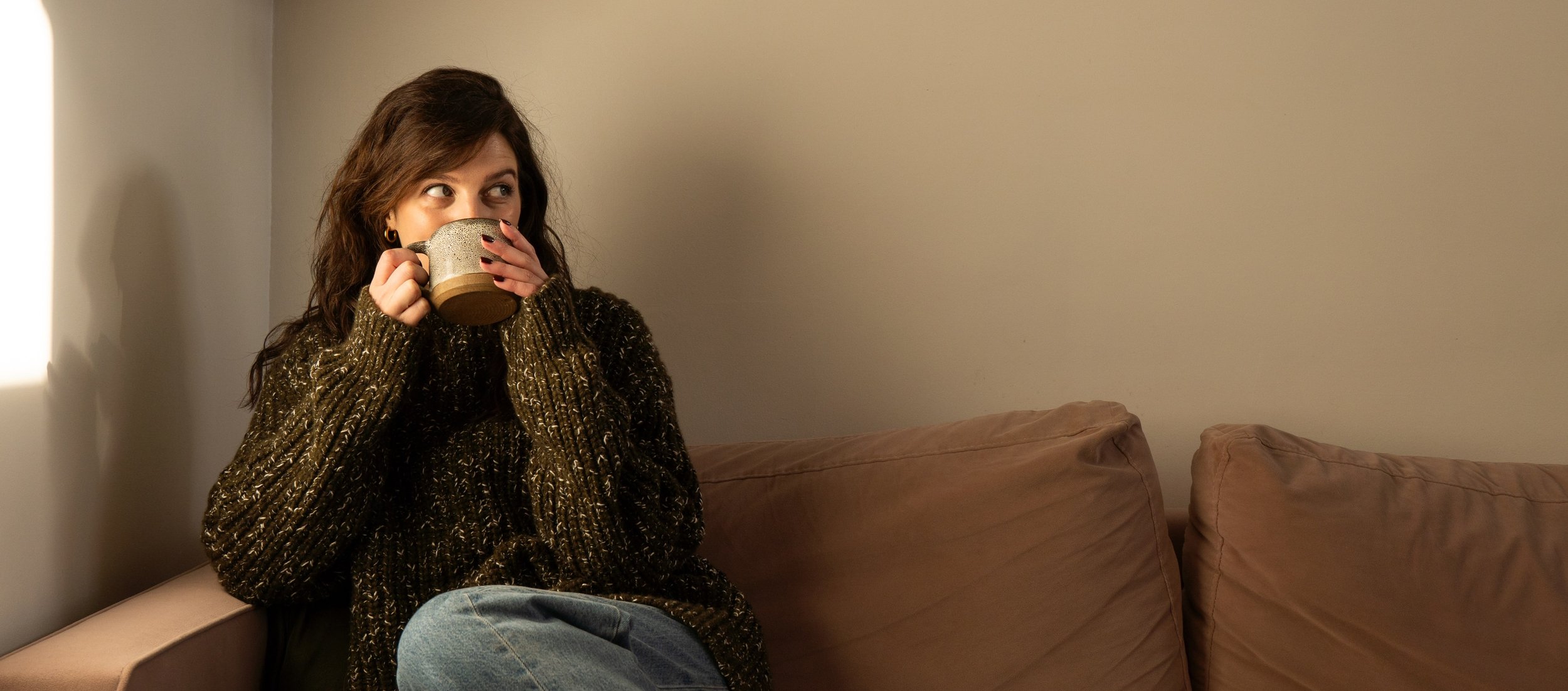 Lifestyle copywriter Hols drinking a cup of tea on the sofa.