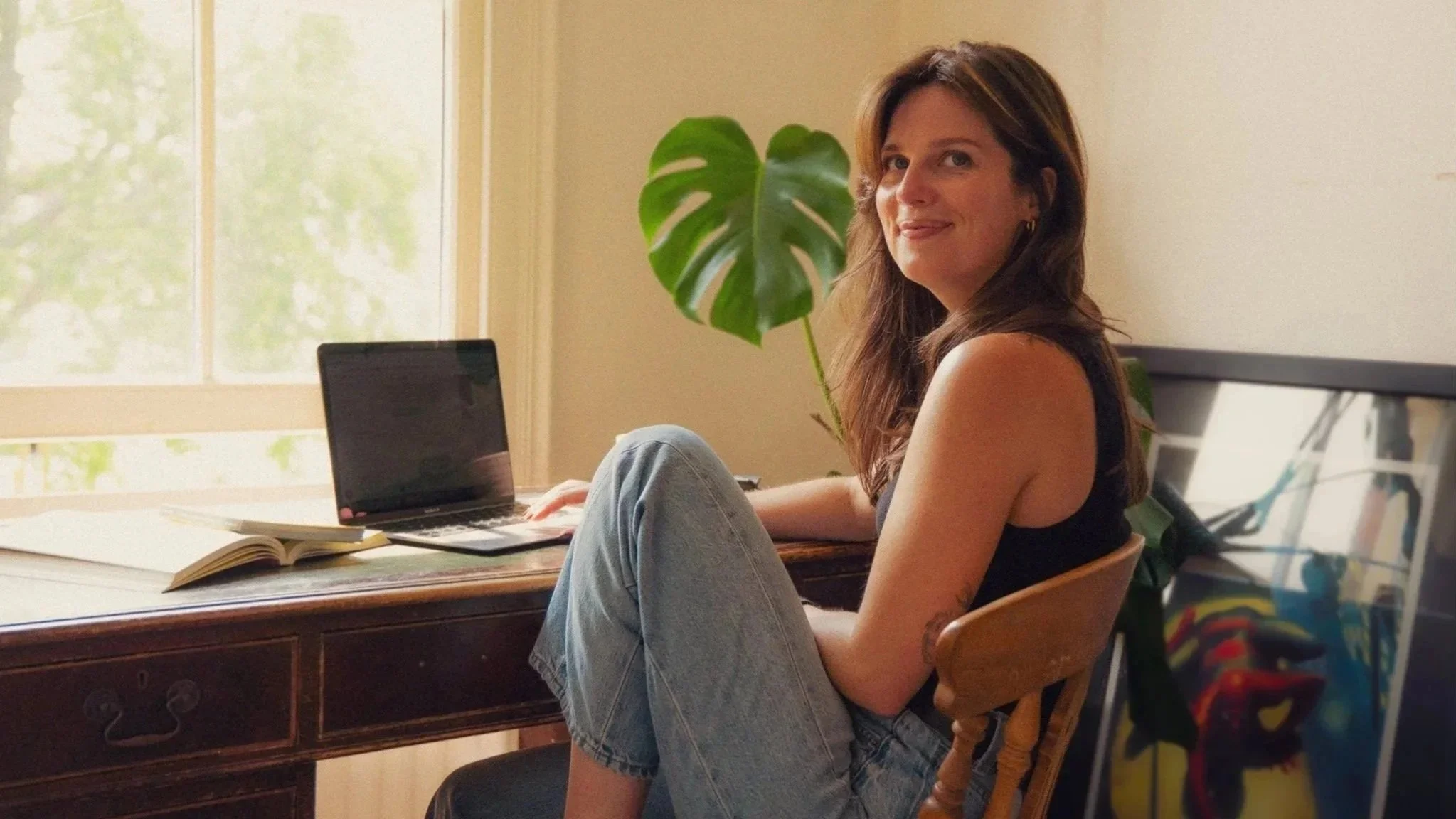 Hols, brand voice strategist looking at the camera, sat at a desk with a laptop and open books