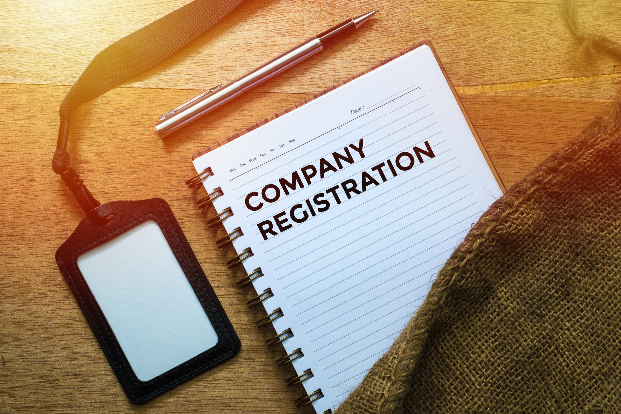 Notepad with "Company Registration" text, blank ID badge, and pen on wooden surface.