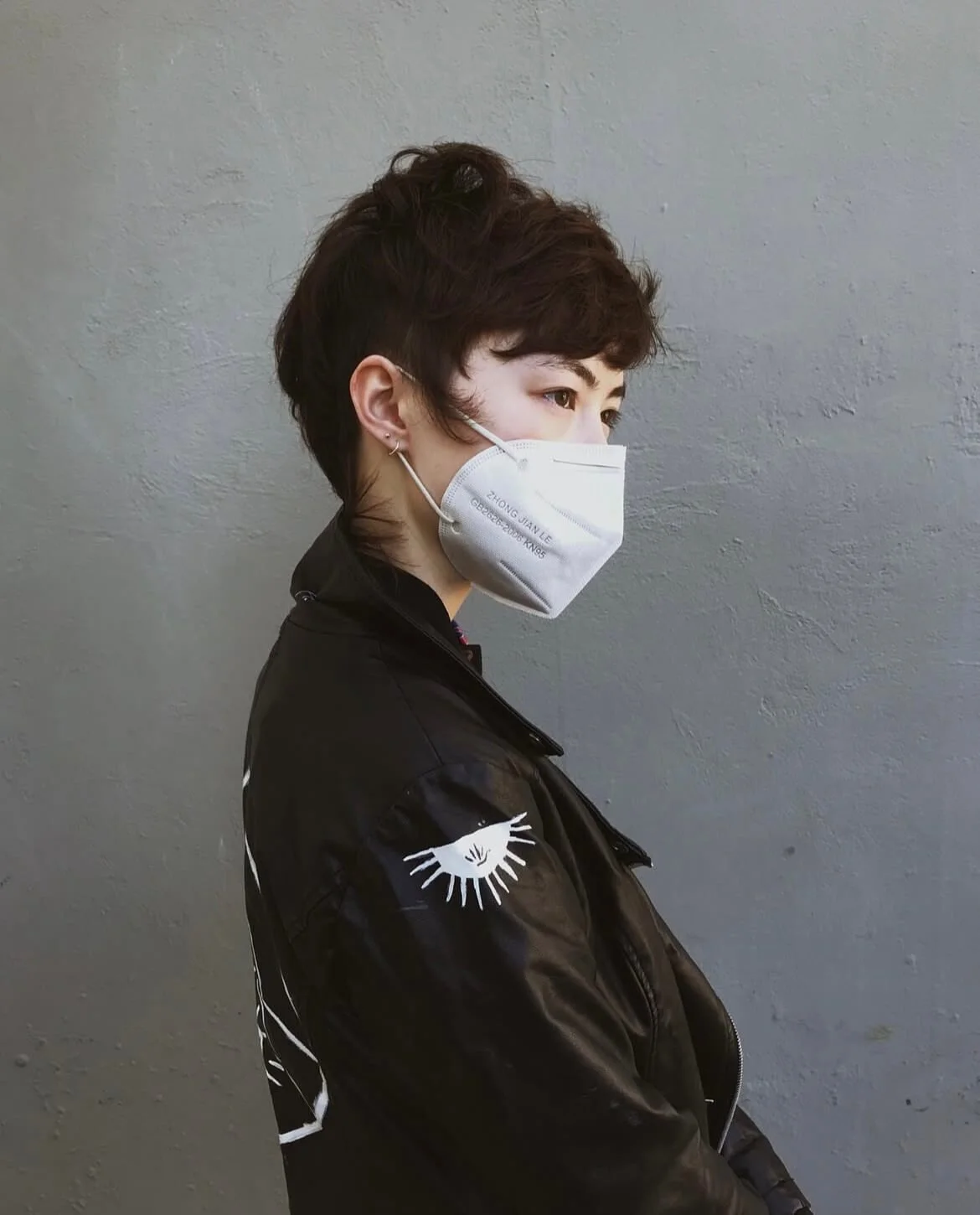 Person wearing a face mask and black jacket with eye design on sleeve