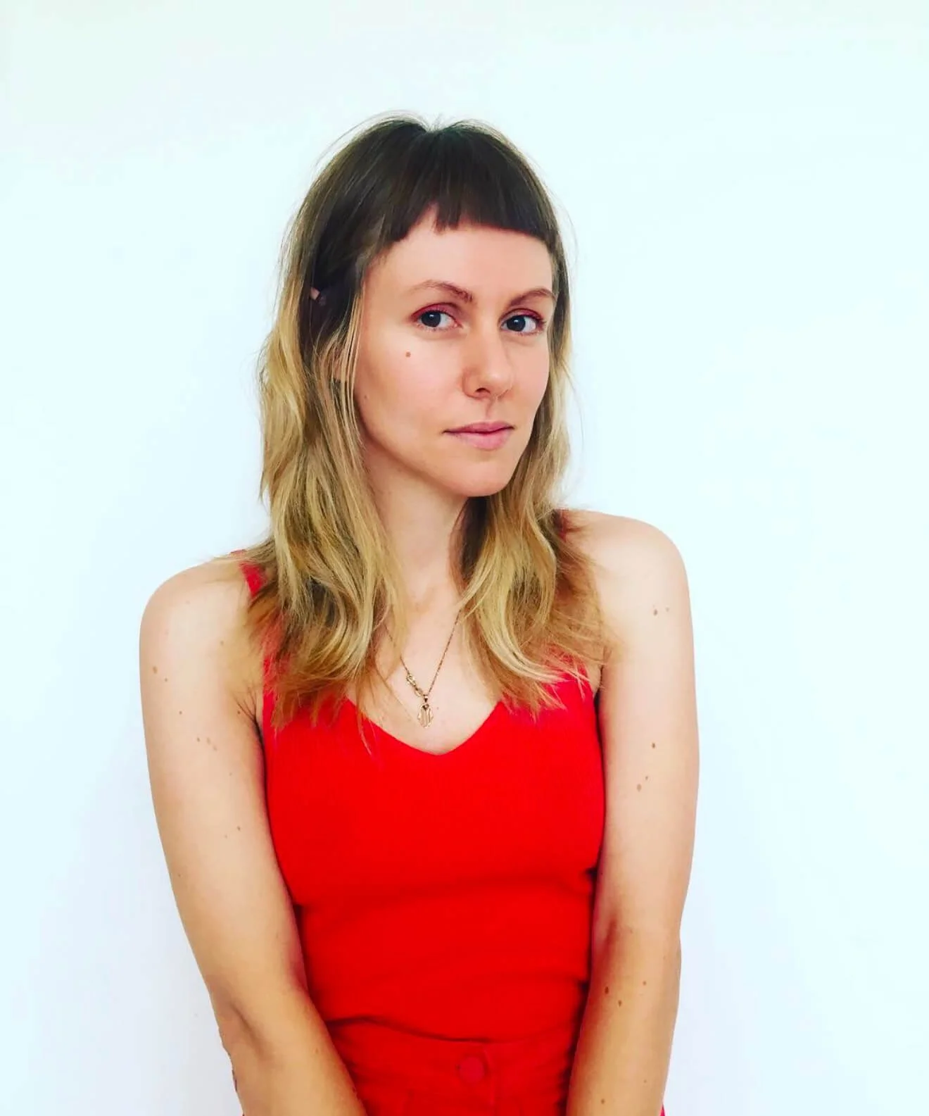 Person with long hair and bangs wearing a red sleeveless top against a white background.