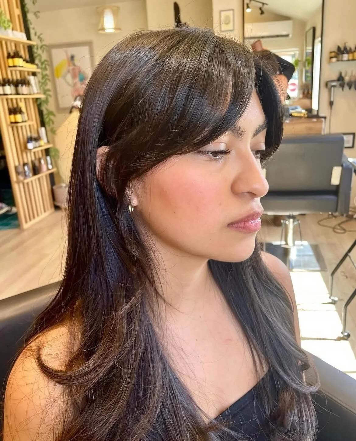 Woman with long black hair in a salon, side profile view.
