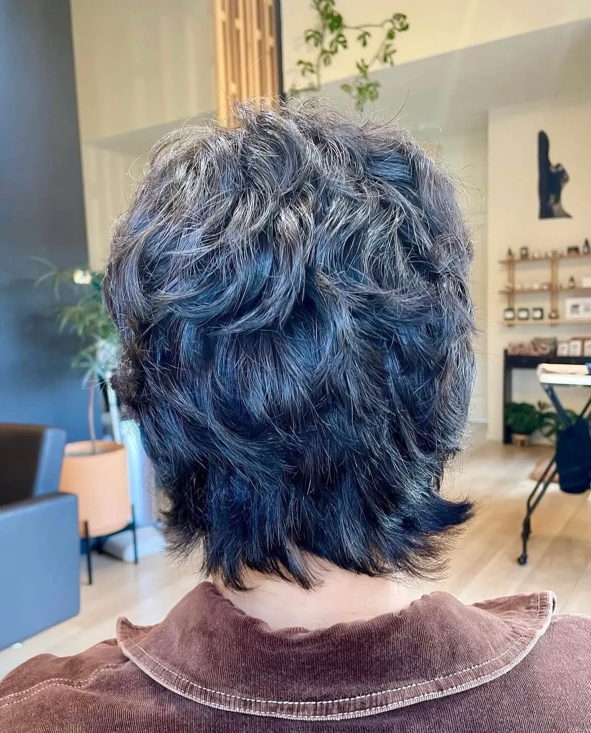 Person with short wavy hair seen from the back inside a salon.
