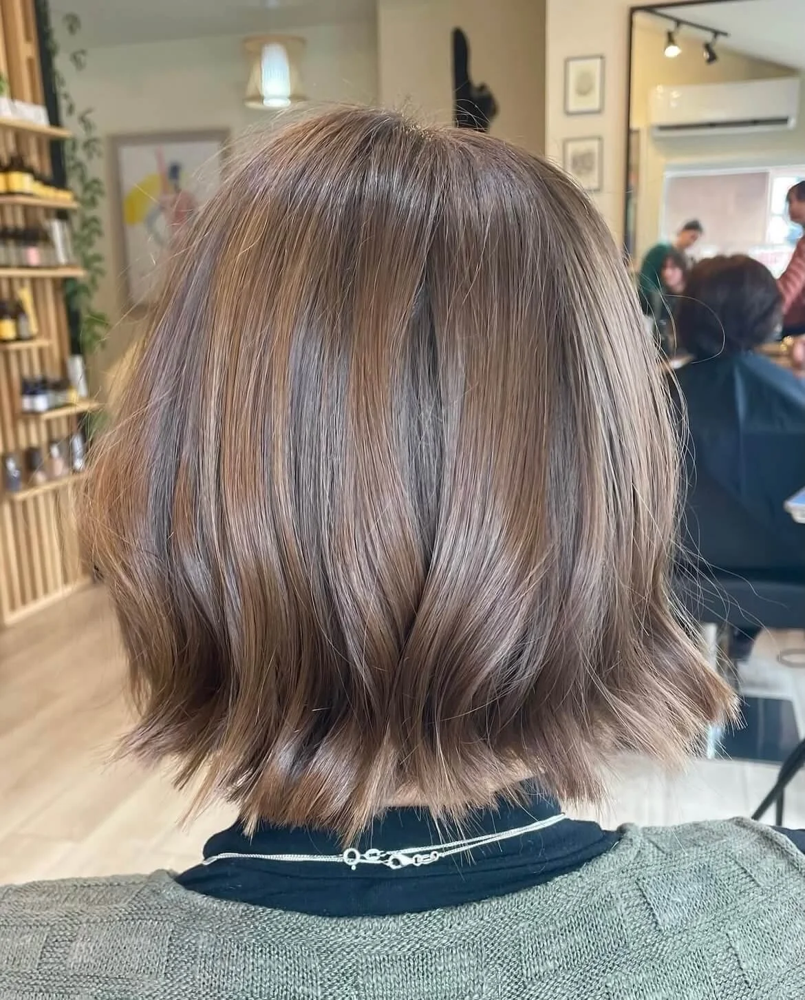 Back view of a person with a short, light brown bob haircut in a salon setting.
