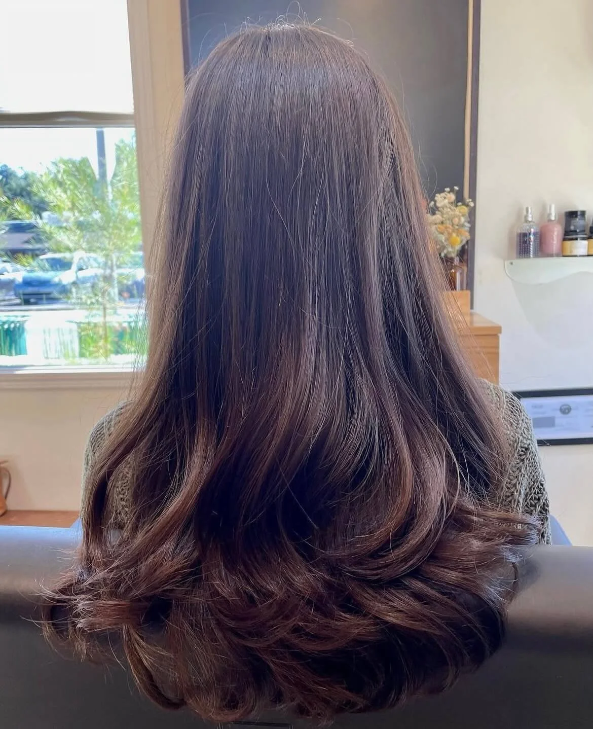 Back view of a person with long, straight brown hair sitting in a salon.