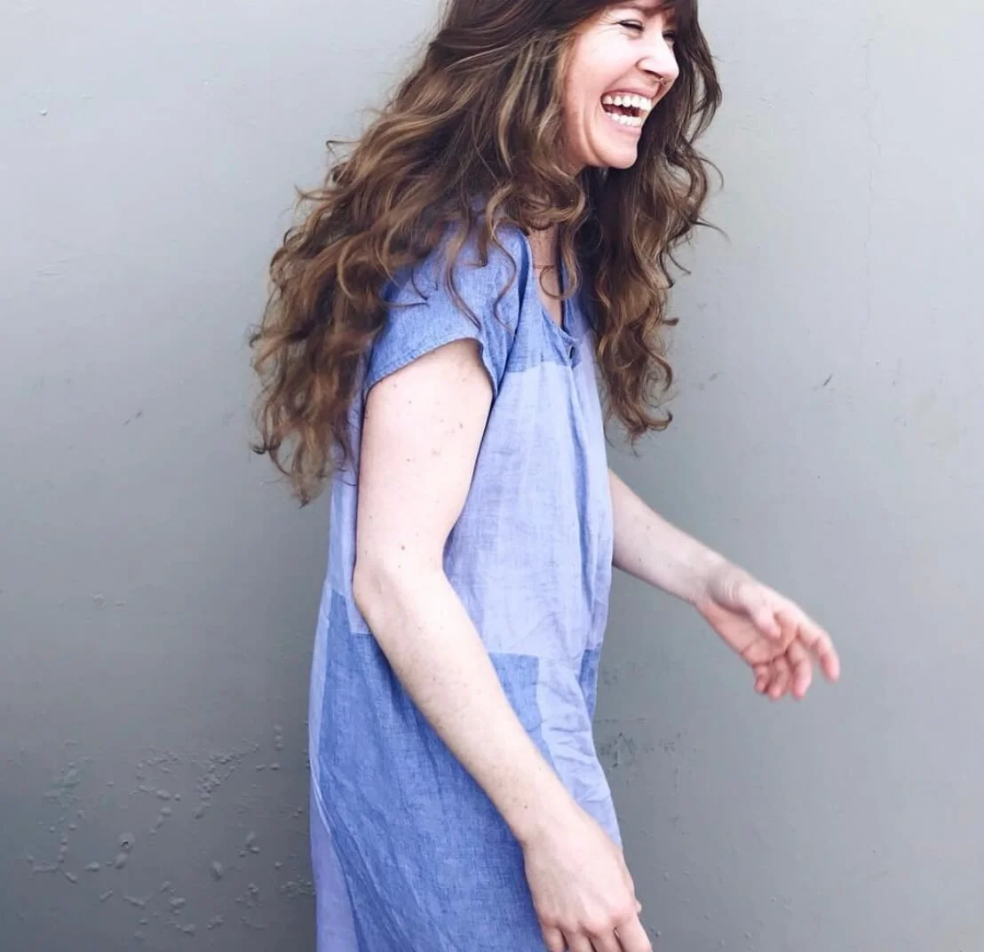 Woman in a casual blue dress laughing against a gray background