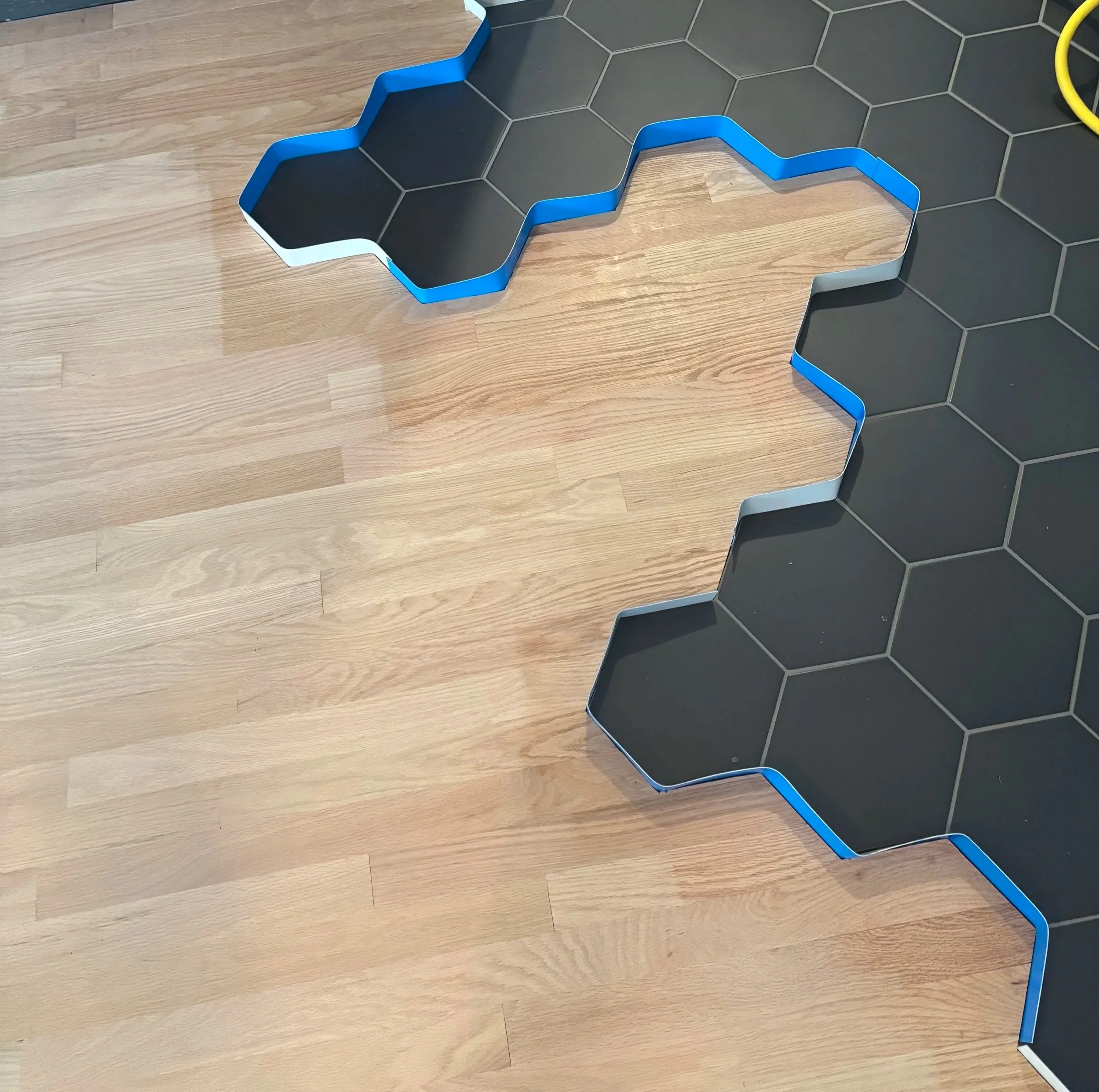 A puzzle piece-shaped black and blue tile mat on a wooden floor, partially surrounded by hexagonal black tiles.
