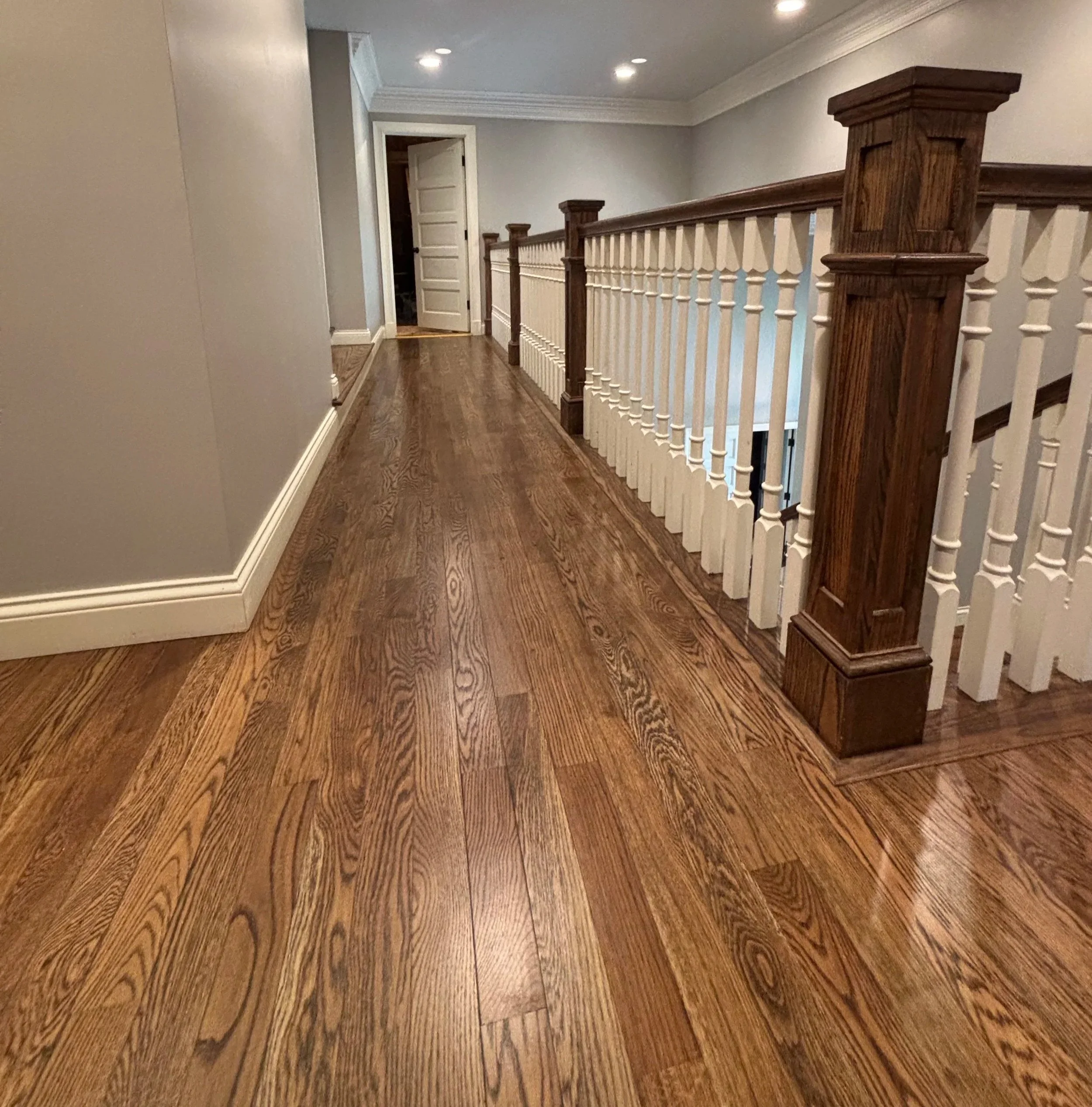 Interior hallway with polished hardwood flooring, gray walls, white baseboards, and a wooden staircase railing.