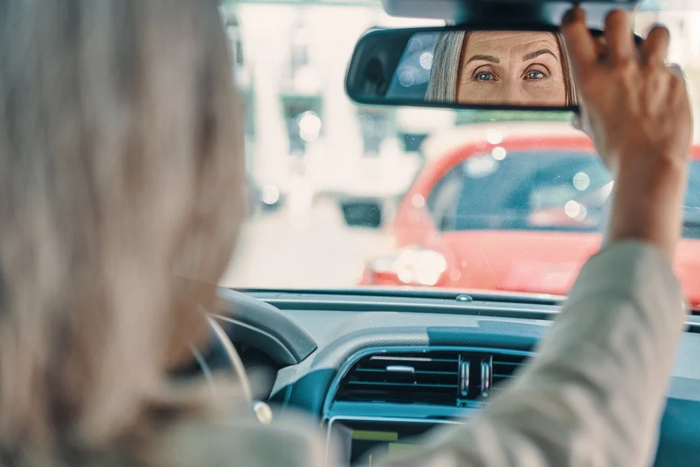 A driver adjusting the rear view mirror in a car.