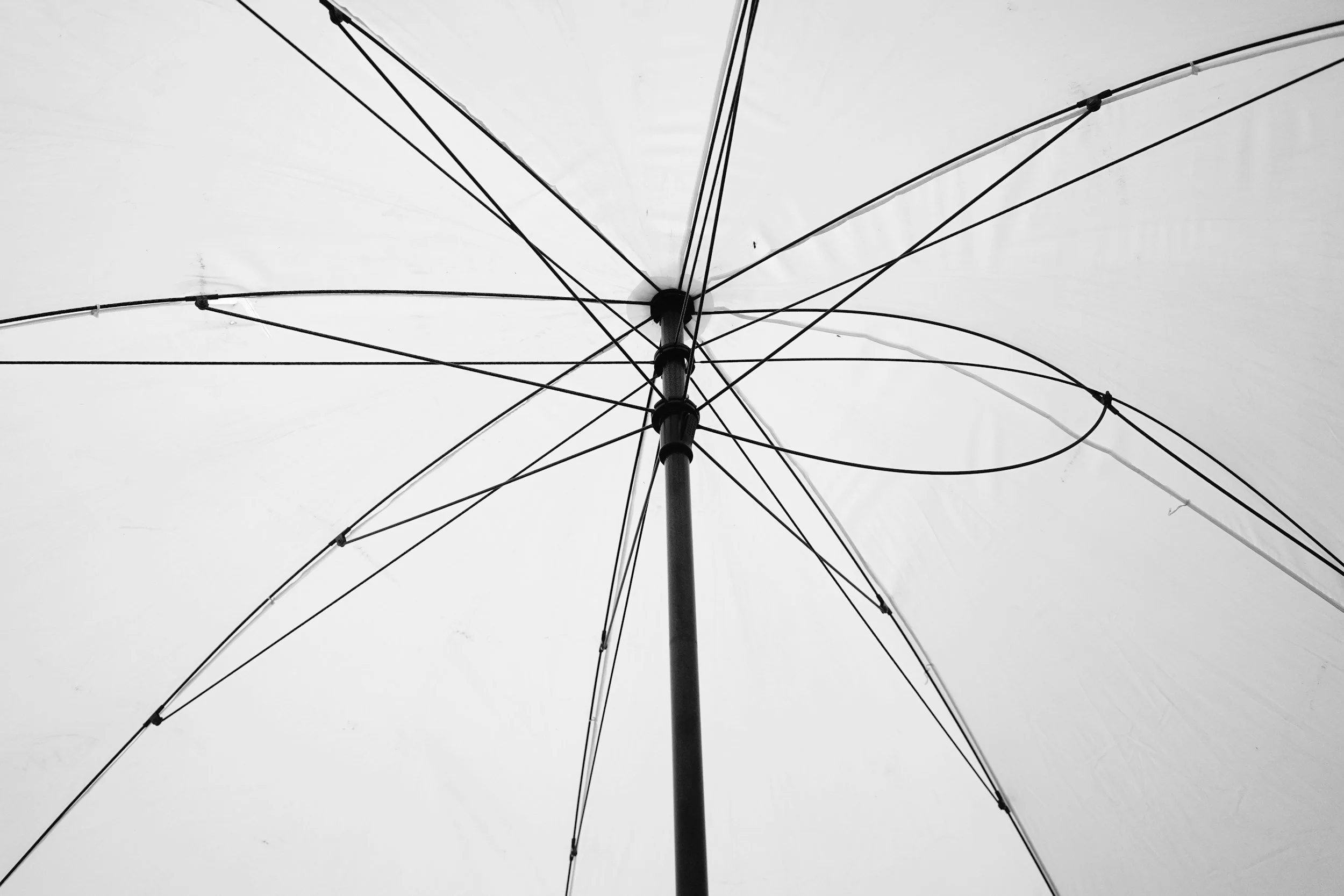 Black and white photo of an open umbrella viewed from underneath, showing the spokes and central pole.