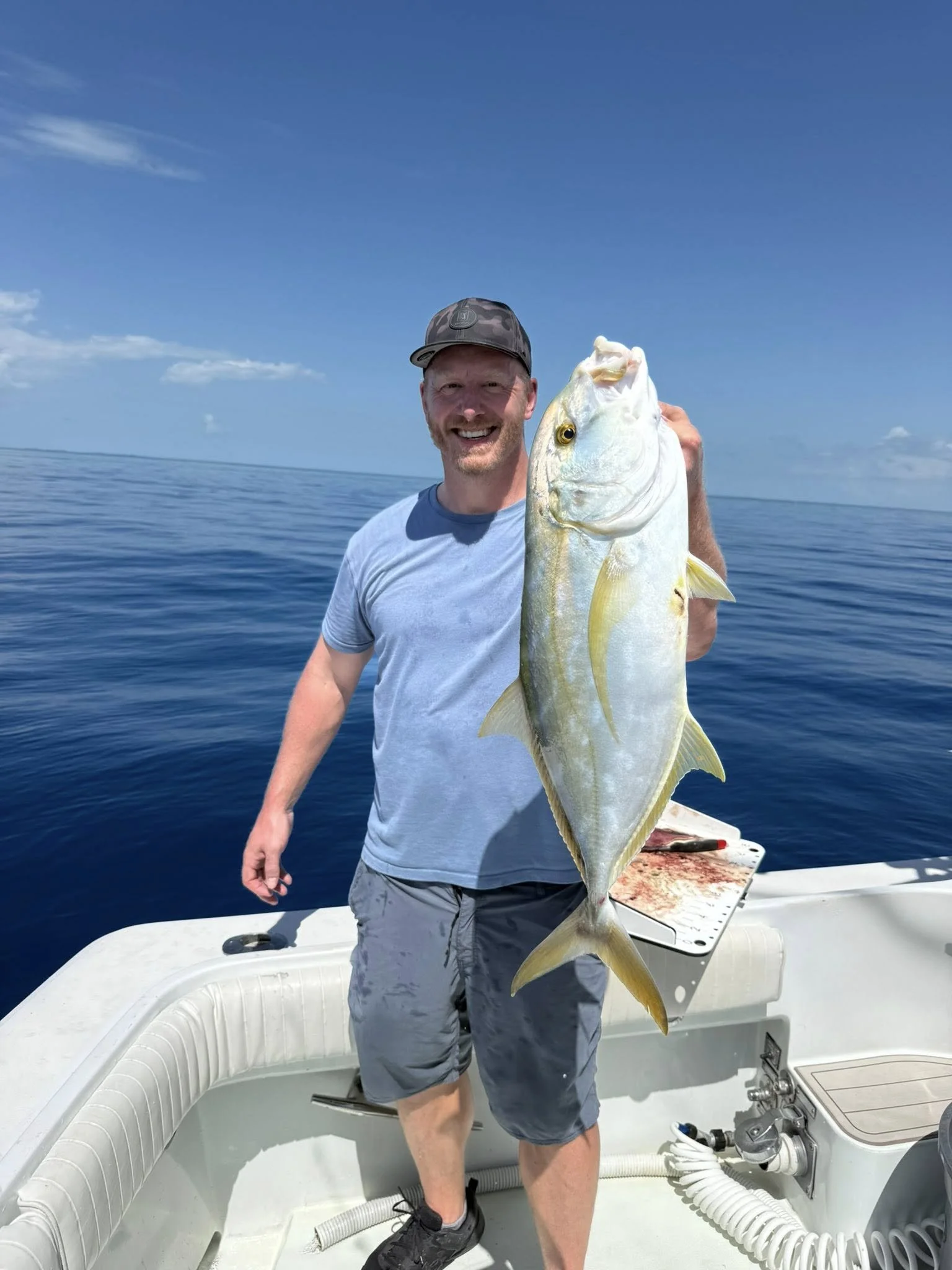 A man smiling and holding a large fish on a boat in the open ocean under a blue sky.