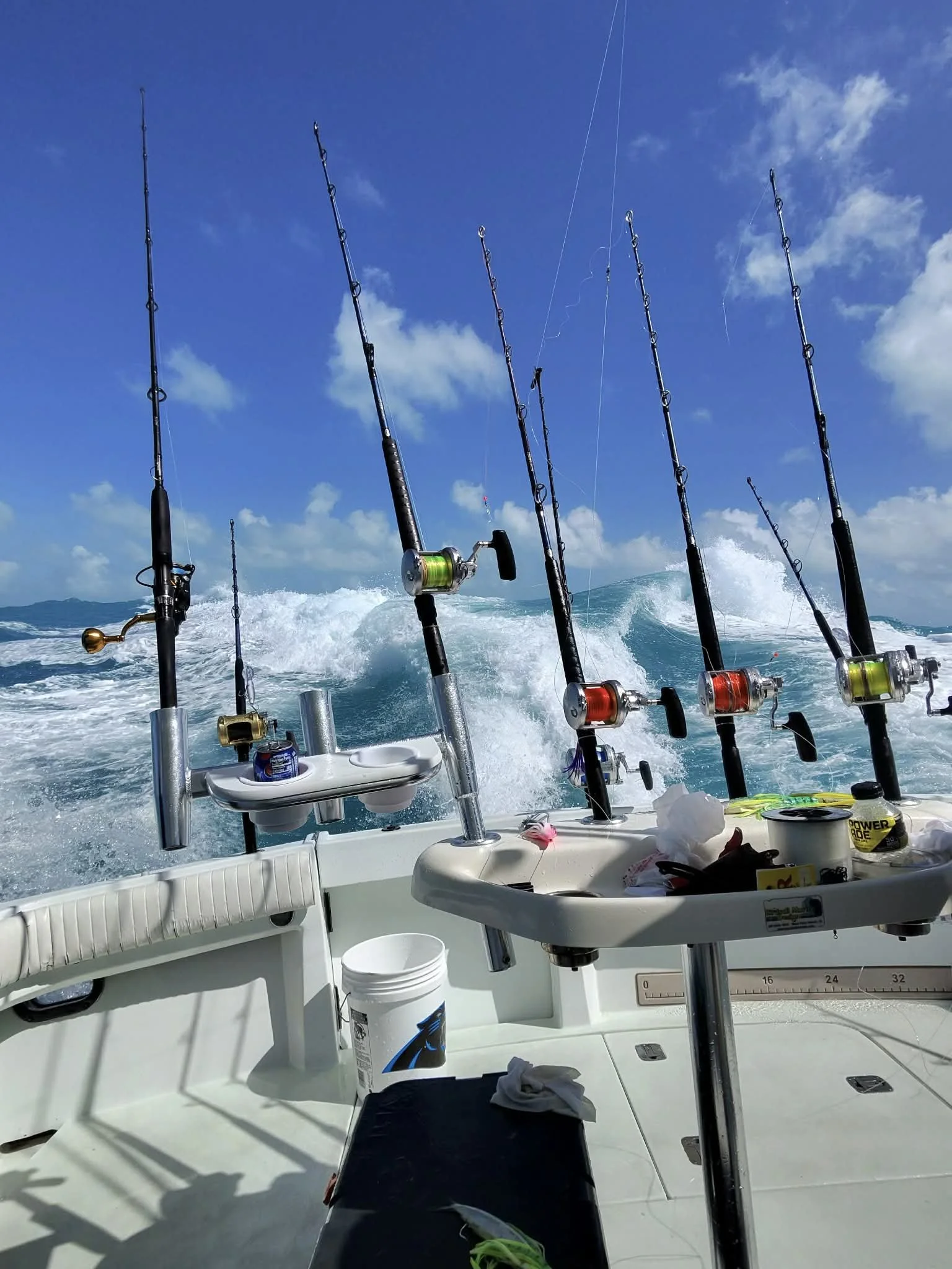 Multiple fishing rods mounted on a boat with ocean waves and blue sky in the background.