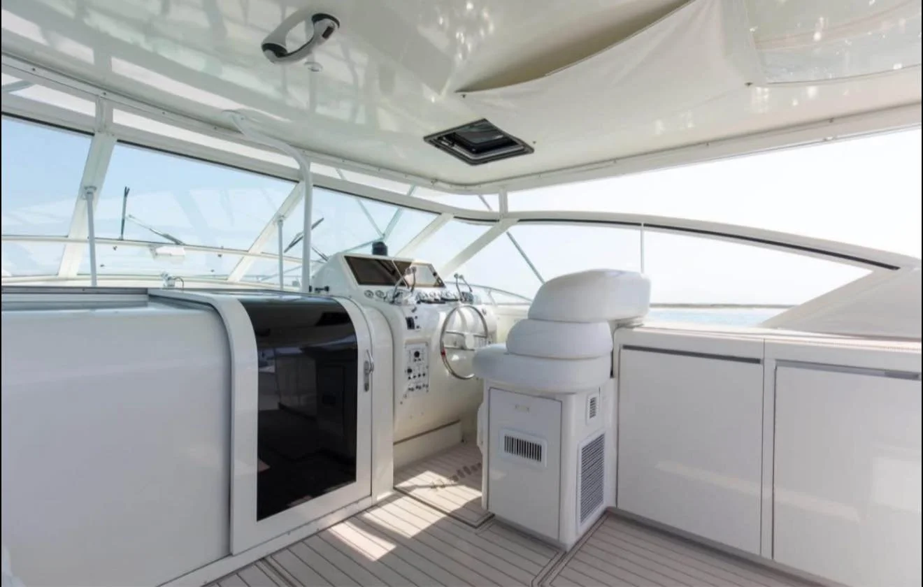 The image shows the interior of a yacht helm station with navigation instruments, a beige captain's chair, and large windows overlooking the ocean.
