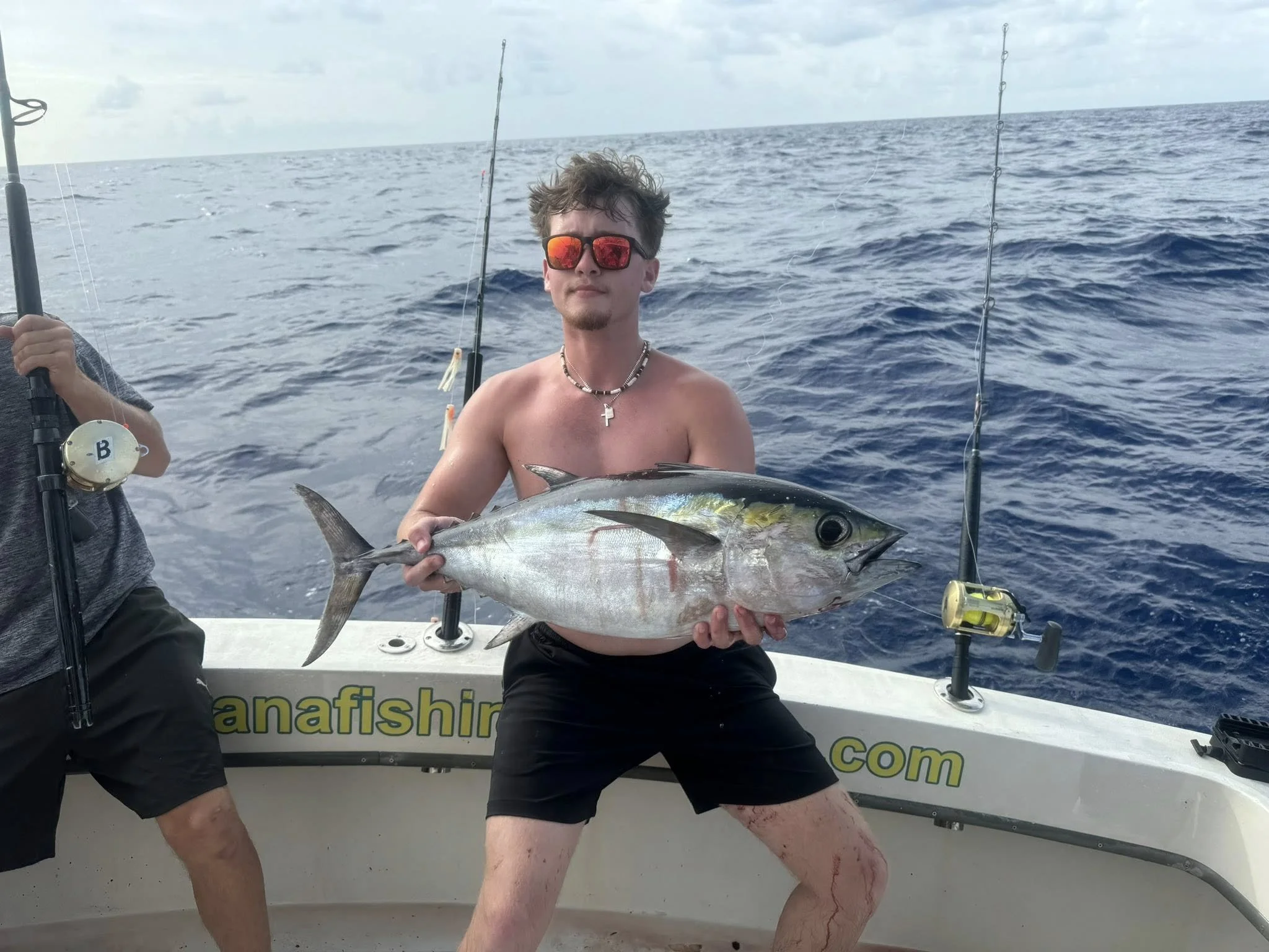 A man holding a large fish on a boat in the ocean, with fishing rods and a cloudy sky in the background.