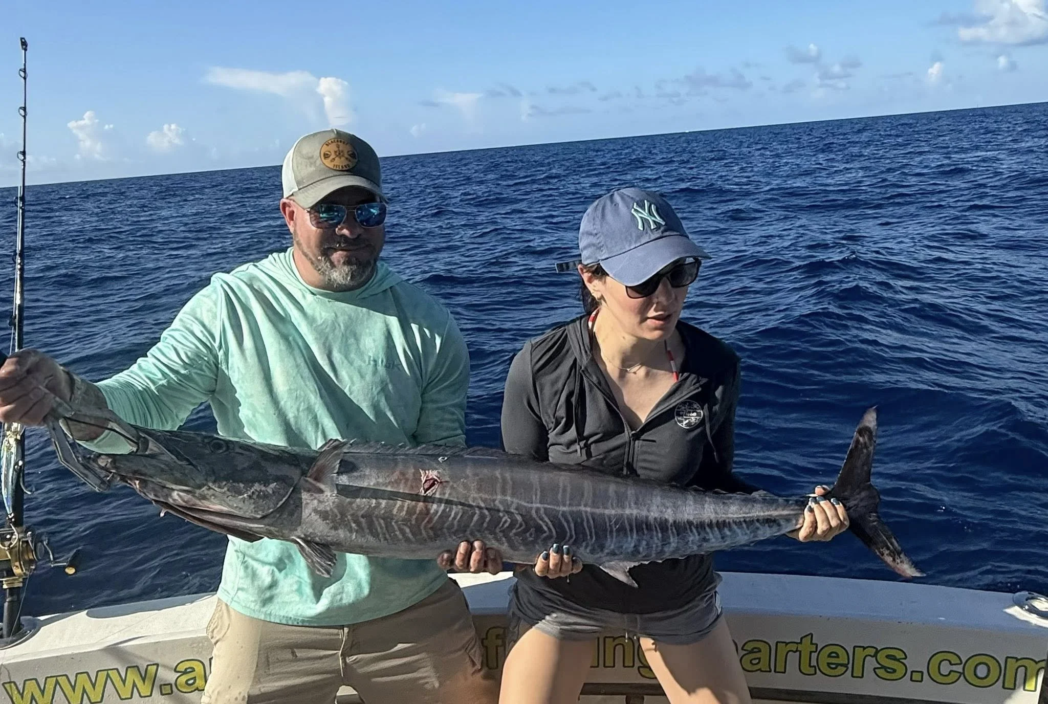 Two people holding a large striped marlin on a boat in the open ocean under a partly cloudy sky.