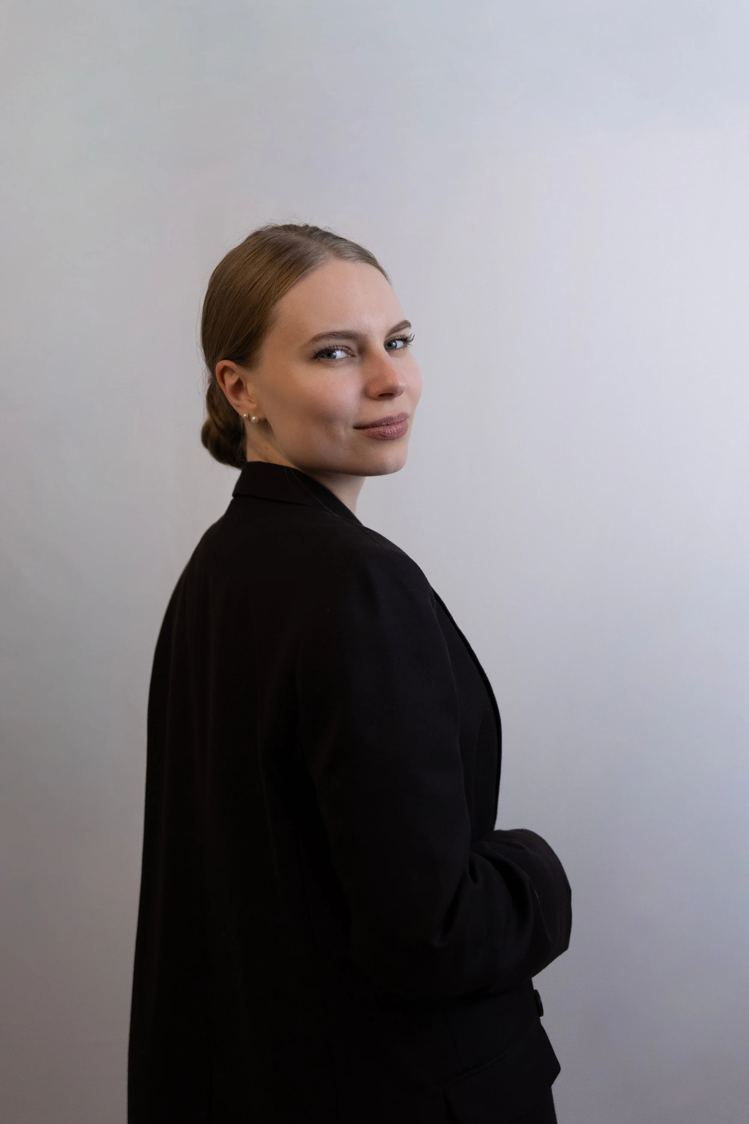 Porträt einer jungen Frau mit rotbraunen Haaren, die nach rechts blickt, vor einem neutral grauen Hintergrund, trägt eine schwarze Jacke.
